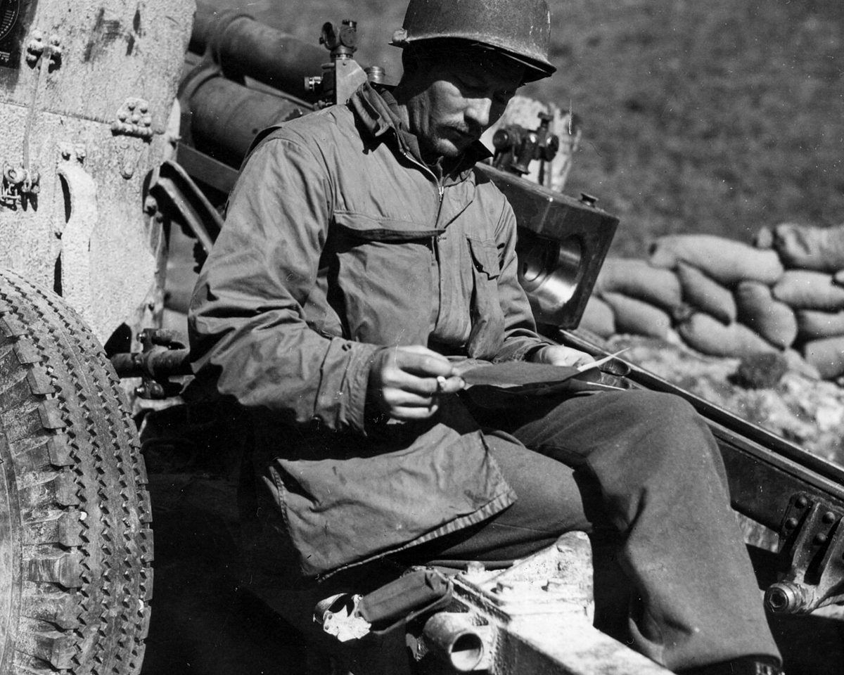 A U.S. Army sergeant reading his first letter from home at a frontline gun position, Italy, 1945